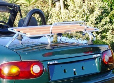 green mazda mx5 mk1 with the hood down next to a hedge with a wood and chrome boot rack fitted