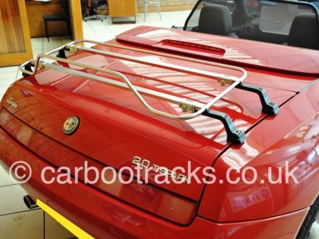side view of a red alfa romeo spider 916 in s showroom with a stainless steel luggage rack fitted to the boot
