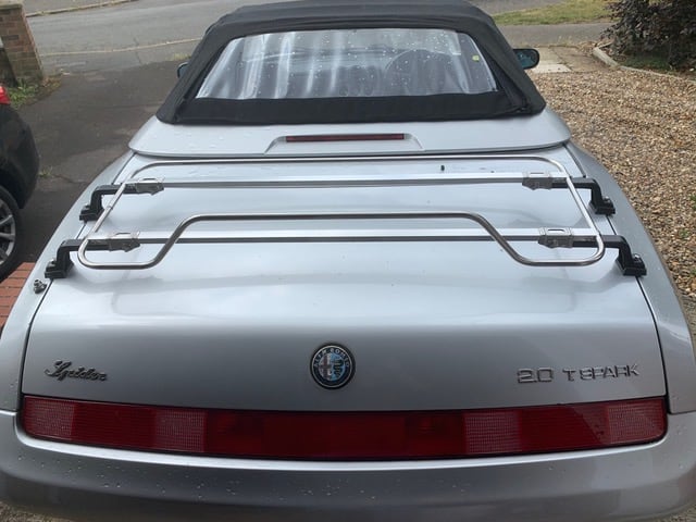 silver alfa romeo 916 spider with a stainless steel luggage rack fitted photographed from behind on a gravel drive