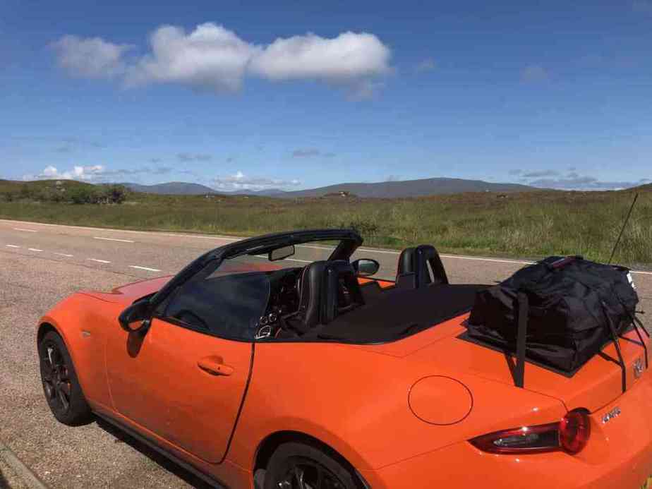Orange mazda mx5 mk4 on a mountain road with a boot rack fitted hod down