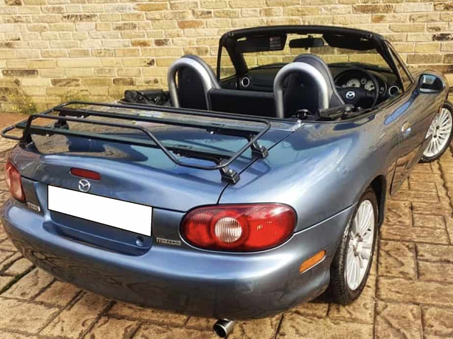 blue mazda mx5 mk2 with a black boot rack fitted roof down on a sunny day by a house
