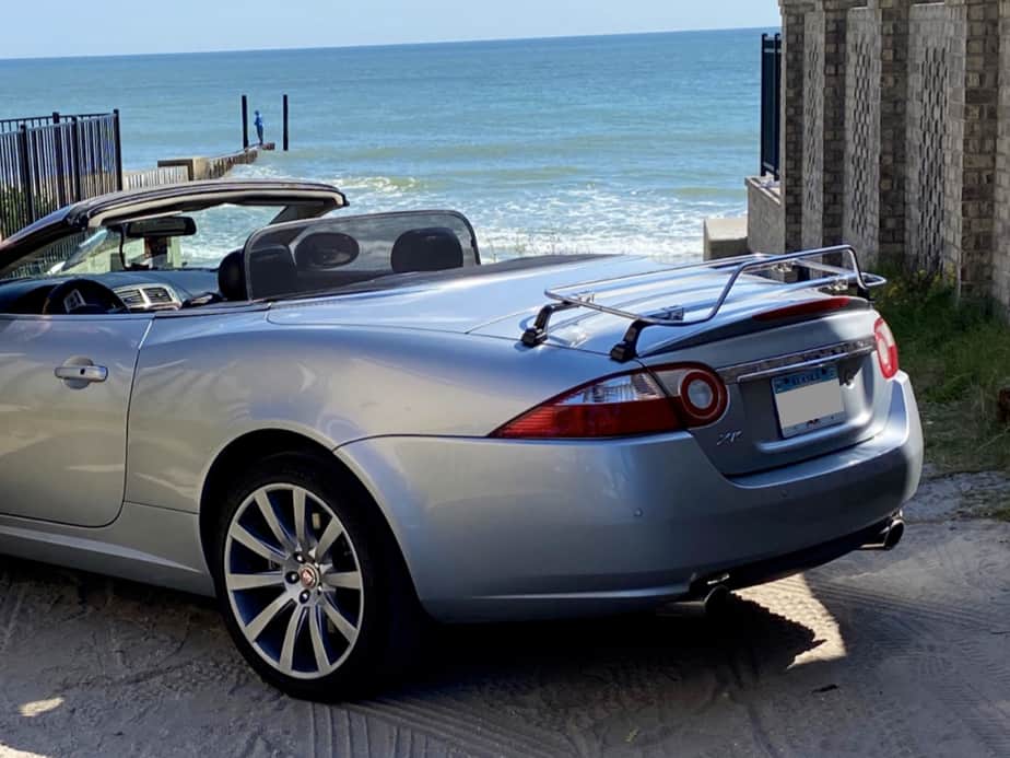 silver jaguar xk convertible with a stainless steel luggage rack fitted on a slipway next to the ocean