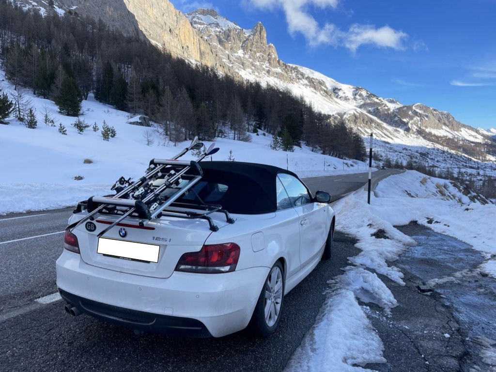 white bmw 1 series convertible on a mountain road with a luggage rack fitted carrying skis