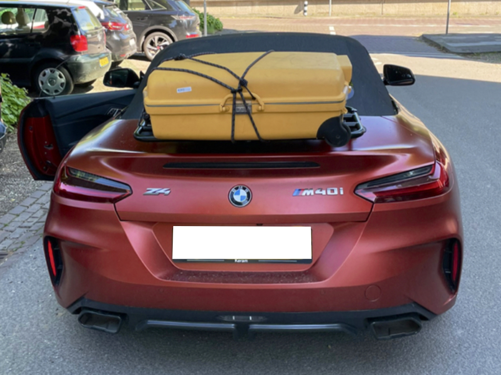 bronze bmw z4 g29 with a luggage rack fitted carrying a large yellow suitcase photographed from the rear in a car park