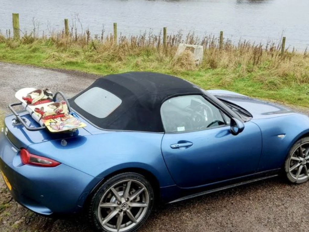 blue mazda mx5 mkw with a boot rack fitted carrying a wakeboard next to a lake